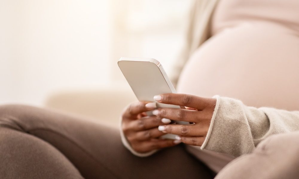 Cropped of pregnant black woman sitting on couch, using smartphone New app launched in US to improve maternal health
