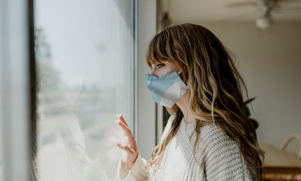 Woman wearing a mask staring out the window during a lockdown Pandemic disrupted women’s health more than men’s, study finds