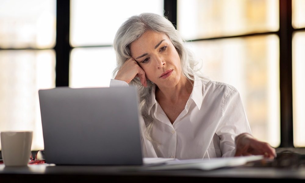Stressed Businesswoman Using Laptop Looking Through Papers Working In Office Nearly a third of UK women consider quitting job due to menopause