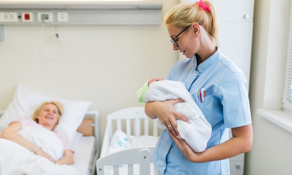 young-nurse-standing-maternity-ward-holding-newborn-baby-her-arms-after-birth-concept The 4th trimester and the new standard in postnatal care