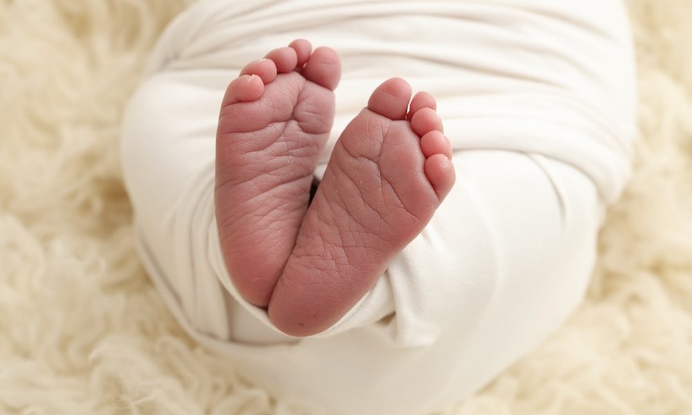 The tiny foot of a newborn baby. Soft feet of a new born in a white blanket. Close up of toes, heels and feet of a newborn. Macro photography. Onto Health acquires diagnostics software company Levy Health