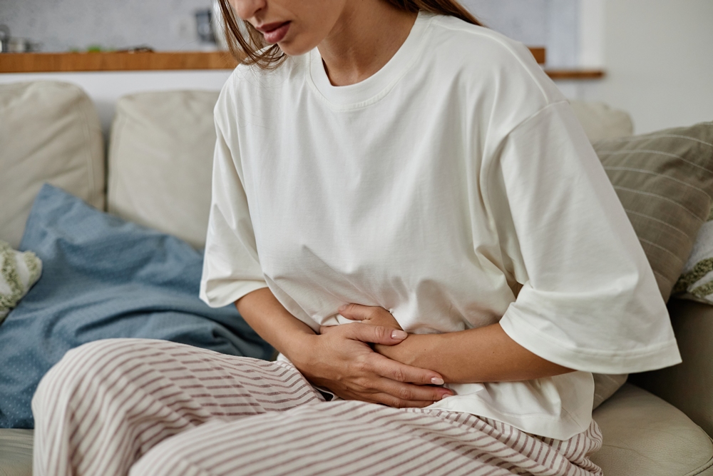 Young Woman Sitting Indoors Holding Stomach in Pain New study explores role of exercise in managing endometriosis pain